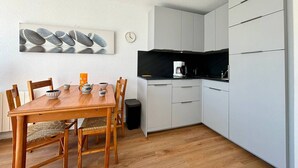 Una cocina compacta con armarios blancos, una mesa de comedor de madera y una encimera negra.