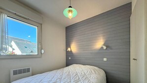 Un dormitorio con cama, ventana, luz empotrada y rejilla de ventilación.