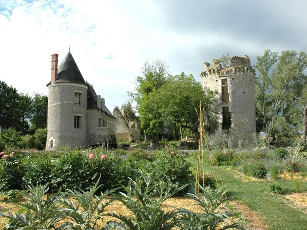 A historic stone building with a tower and a round tower, surrounded by lush gardens and trees.