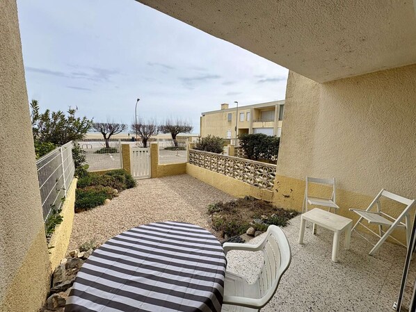 Un balcon avec une table et des chaises à rayures, une vue sur un immeuble et un sol recouvert de gravier.