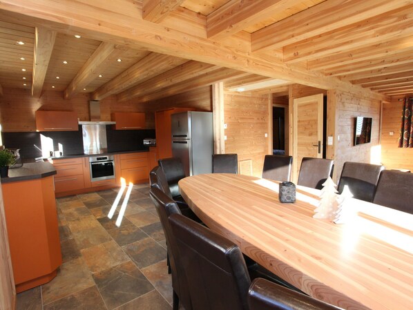 Una cocina moderna con armarios de madera, una isla central y un comedor con una gran mesa y sillas de madera.