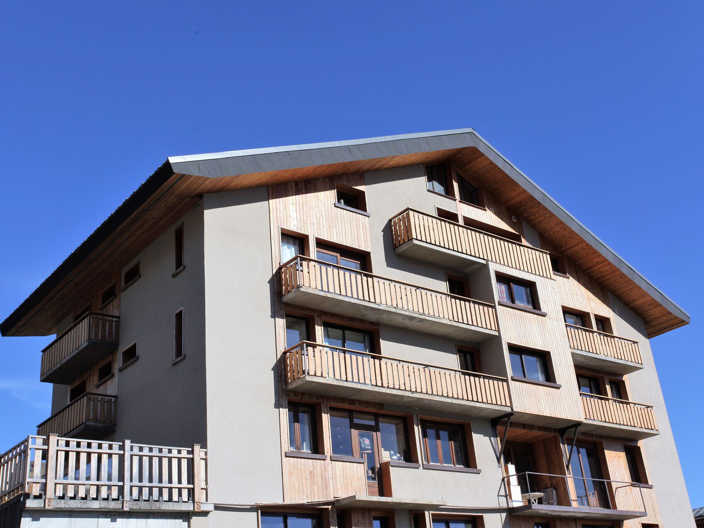 Ein mehrstöckiges Gebäude mit Balkonen, einer flachen Dachterrasse und blauem Himmel.