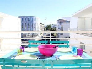 A balcony with a table set for two, featuring a pink bowl and various glassware.