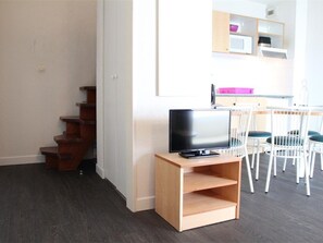 A room with a wooden TV stand, a flat-screen TV, a dining table with white chairs, and a staircase.