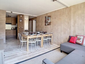 Uma sala de estar moderna com um sofá cinza, uma mesa de jantar com cadeiras e uma área de cozinha com armários de madeira.