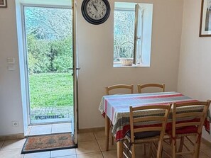 Un coin repas avec une table dressée pour quatre personnes, une horloge au mur et une fenêtre donnant sur un jardin.