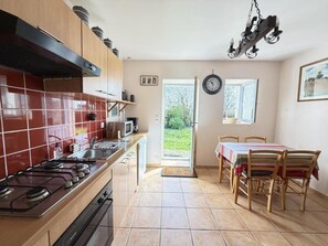 Une cuisine équipée d’une cuisinière à gaz, d’un four à micro-ondes et de meubles en bois. On y trouve également un coin repas avec une table et des chaises, ainsi qu’une fenêtre donnant sur un espace verdoyant.