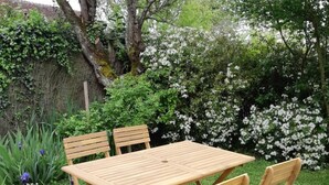 A wooden table and four chairs in a garden with flowering bushes and a hedge. - Charming cottage with garden, near Chenonceau and Beauval (Luzillé)