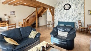 A living room with a wooden ceiling, a blue leather sofa, a blue armchair, a coffee table, and a wall clock. - Charming cottage with garden, near Chenonceau and Beauval (Luzillé)