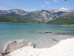 A clear lake with a rocky shoreline and mountains in the background.