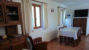 Un coin repas comprenant une table et des chaises, un canapé, un meuble avec des portes en verre et un téléviseur posé sur un meuble.