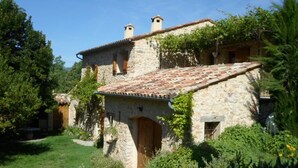 Un bâtiment en pierre avec un toit en tuiles, entouré de verdure et d’arbres.