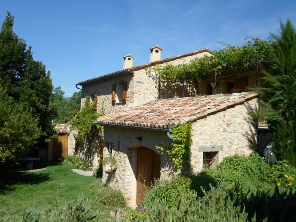 A stone building with a tiled roof, surrounded by greenery and trees.