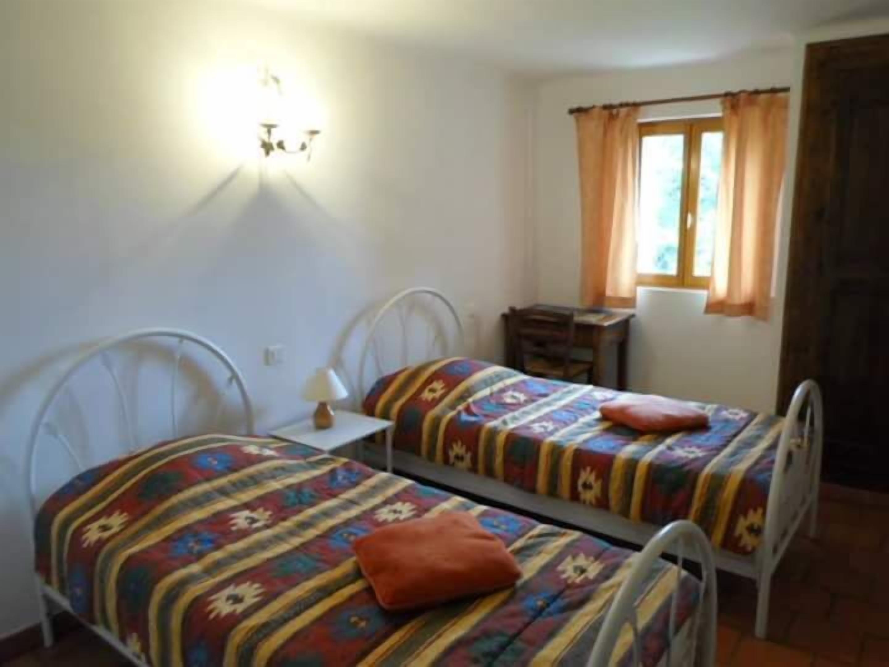 Un dormitorio con dos camas individuales, una mesita de noche, una lámpara, una ventana con cortinas y un aparador de madera.