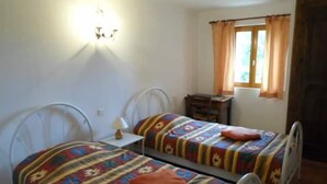 Une chambre avec deux lits simples, une table de chevet, une lampe, une fenêtre avec des rideaux et une commode en bois.