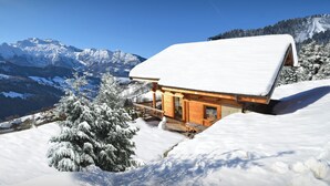 A wooden cabin with a snow-covered roof, surrounded by snow-covered trees and mountains. - Chalet Chocolat - Manigod ski base for 8, log fire nights - OVO Network (Manigod)