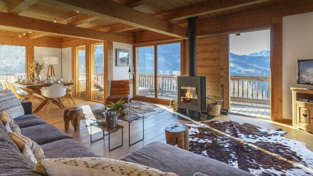 A cozy living room with a large sofa, a fireplace, and a view of mountains. - Chalet Chocolat - Manigod ski base for 8, log fire nights - OVO Network (Manigod)