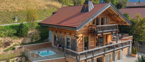 A wooden chalet with a hot tub, a balcony, and a view of mountains.