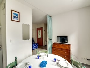 A dining area with a round table set for four, a television on a wooden cabinet, and a door leading to another room.