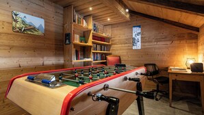 Una habitación acogedora con una mesa de fútbol de mesa, estanterías de madera y un escritorio con una silla.