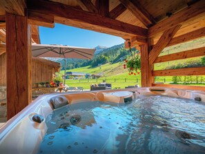 Een hottub met een houten plafond en uitzicht op een bergachtig landschap.
