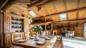 Un comedor de madera con una larga mesa dispuesta para una comida, armarios de madera con vajilla y un techo rústico con tragaluces.