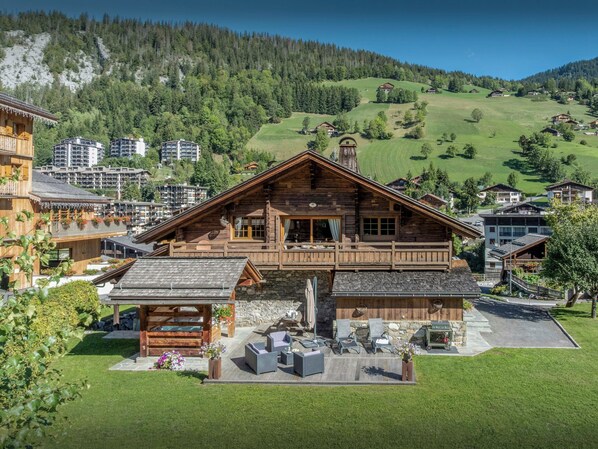 A wooden chalet with a balcony, stone foundation, and outdoor seating area.