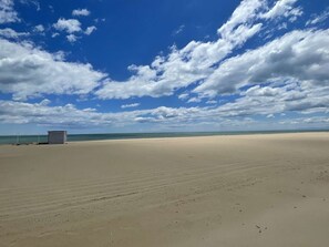 Une plage avec une tour de surveillance, du sable et un ciel dégagé parsemé de nuages.