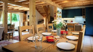 A wooden dining table set with plates, glasses, and a pitcher of water, with a kitchen in the background.