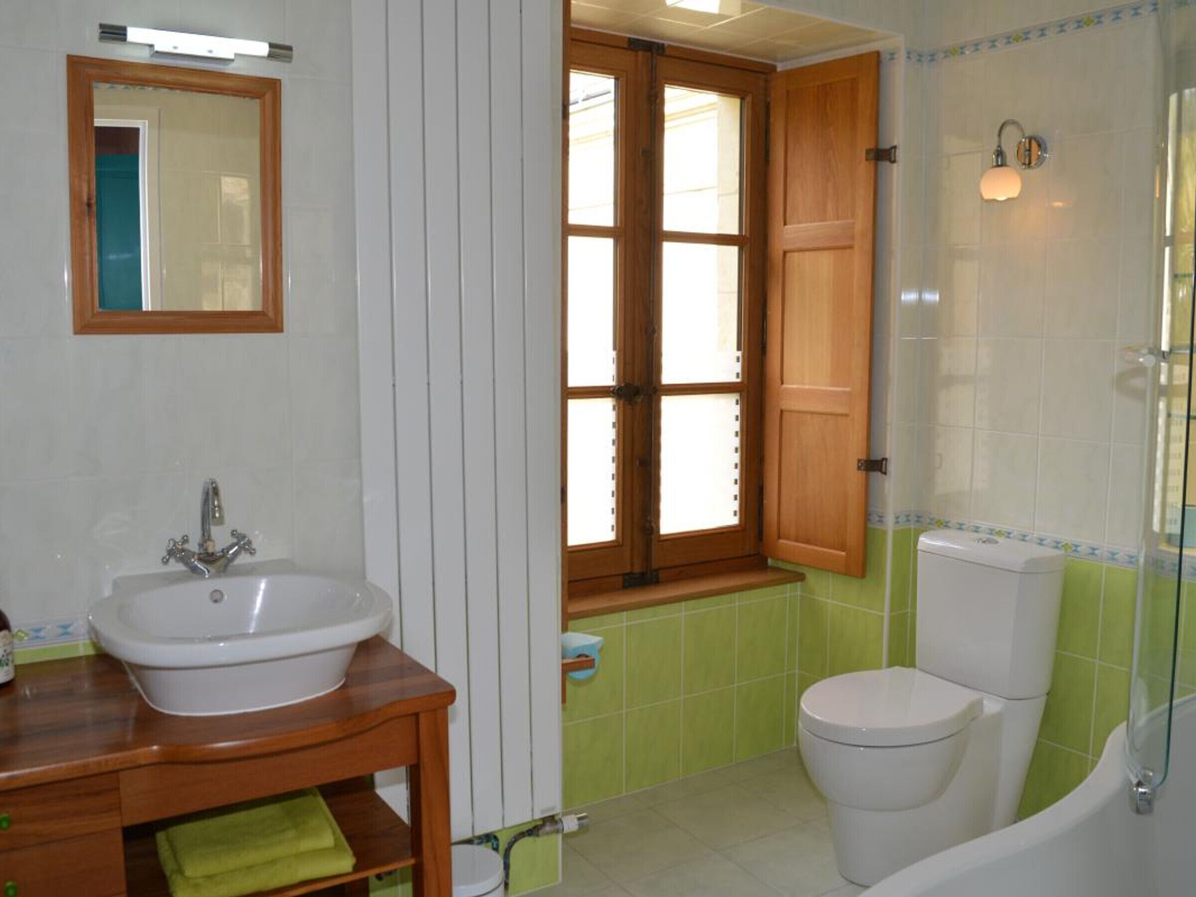 A bathroom with a white sink, wooden vanity, green-tiled walls, a toilet, and a glass-enclosed shower area.