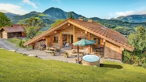 Una cabaña de madera con techo inclinado, un patio con mobiliario exterior y un jacuzzi.