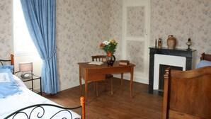 Un dormitorio con papel tapiz floral, una cama de madera, una mesa con un florero y una chimenea.