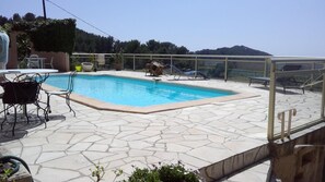 A swimming pool with stone tiles, lounge chairs, and a table.
