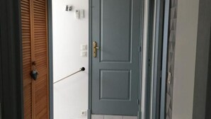 Um corredor com uma porta cinzenta, uma porta de madeira e uma parede branca com um termostato e um interruptor de luz.