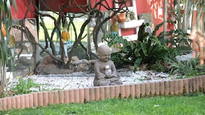 Un jardín con una estatua de Buda, una jaula de pájaros y un edificio rojo al fondo.