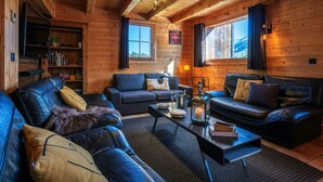 A cozy log cabin interior with leather sofas, a coffee table, and a bookshelf.