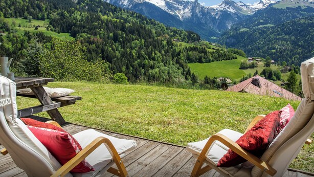 A deck with two lounge chairs and a table, overlooking a mountainous landscape with snow-capped peaks and a valley. - Chalet Chenavray - Manigod base for 10, spa & great skiing - OVO Network (Manigod)