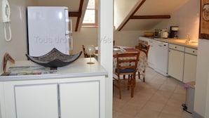 Una cocina con un refrigerador blanco, sillas de madera, una mesa de comedor con mantel de lunares y una lámpara colgante.