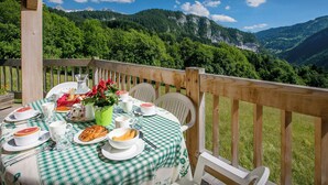 Un área de comedor al aire libre con mantel a cuadros, platos de comida y vistas a las montañas.