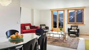 Una sala de estar moderna con un sofá rojo, una mesa de comedor con sillas y un ventanal con vistas a la montaña.