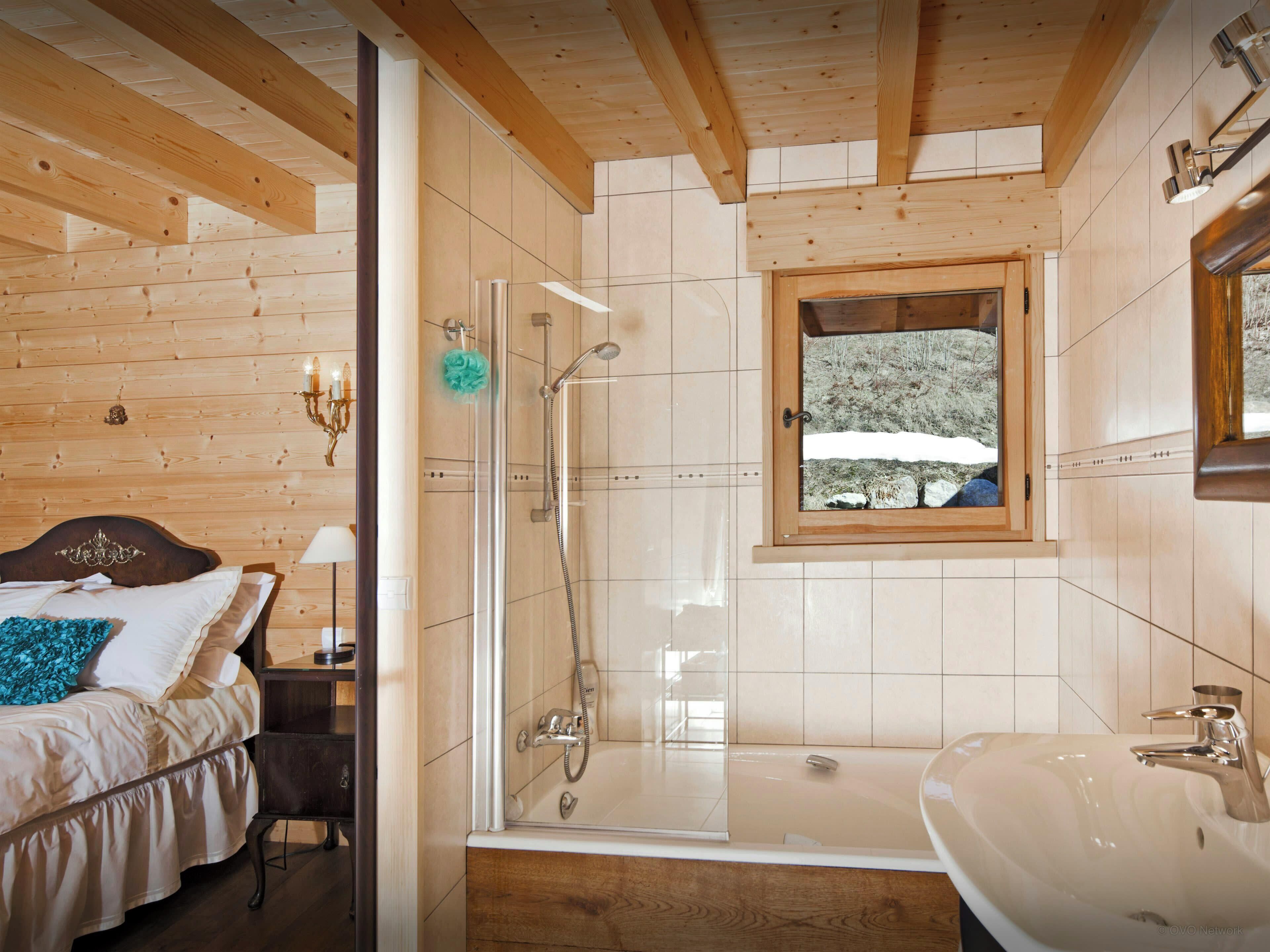 Une salle de bain avec une douche, une baignoire et une fenêtre donnant sur des arbres couverts de neige.