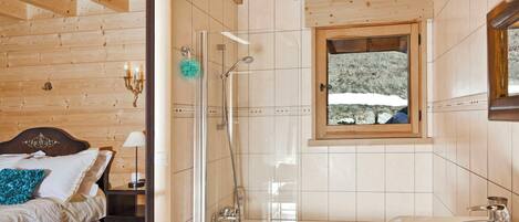 Une salle de bain avec une douche, une baignoire et une fenêtre donnant sur des arbres couverts de neige.