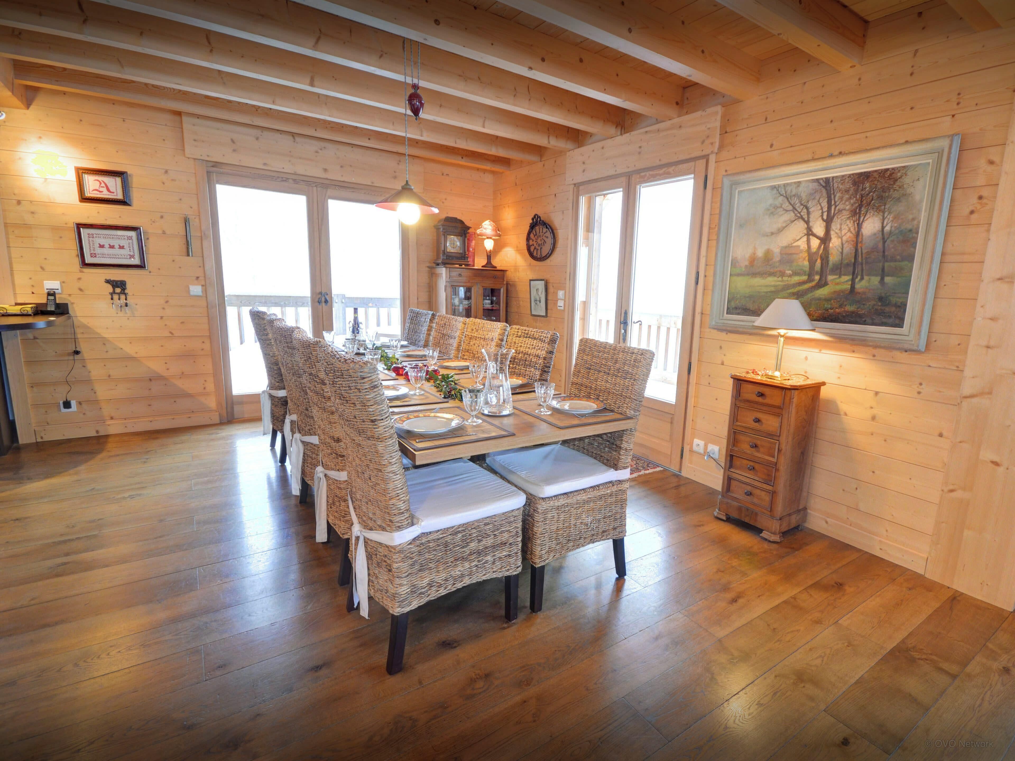 A dining area with a wooden table set for six, surrounded by wicker chairs with white cushions.