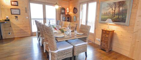 A dining area with a wooden table set for six, surrounded by wicker chairs with white cushions.