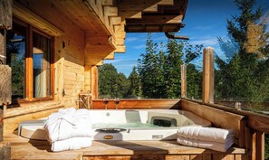 Une cabane en bois avec un jacuzzi, des serviettes et une vue sur les arbres.