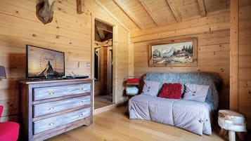 Ein Zimmer in einer Holzhütte mit einem Bett, einem Schminktisch, einem aufgehängten Tierkopf, einem Gemälde und einem Fernseher, der eine Bergbahn zeigt.