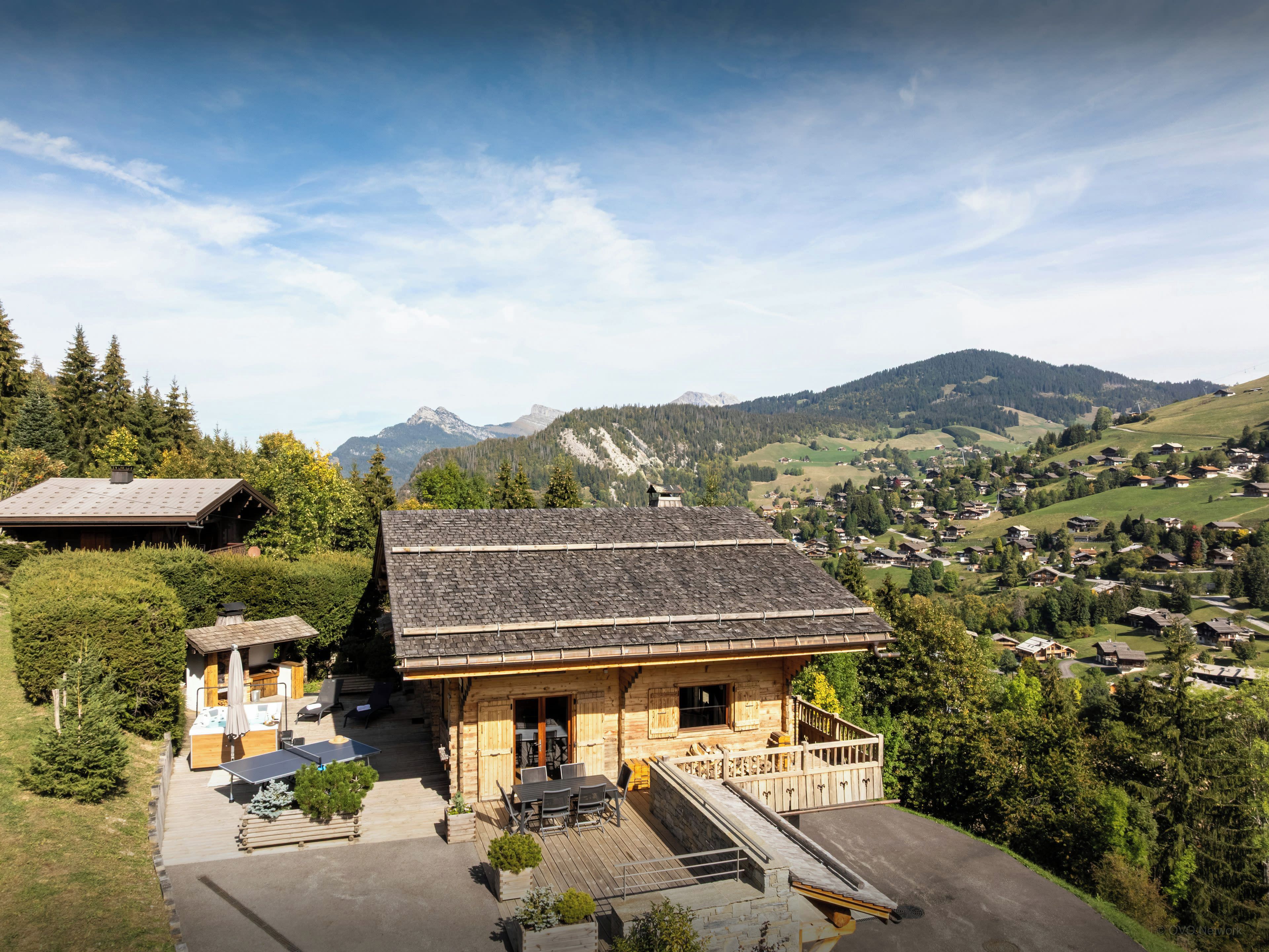 Un chalet doté d’une terrasse, d’un espace salon extérieur et offrant une vue sur un village de montagne.