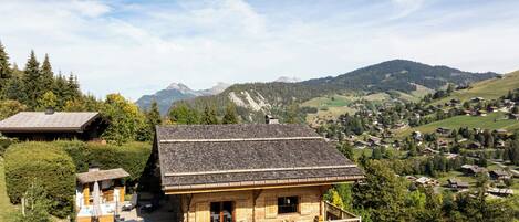 Un chalet doté d’une terrasse, d’un espace salon extérieur et offrant une vue sur un village de montagne.
