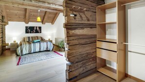 Un dormitorio con techo de madera, una cama con ropa de cama a rayas, una lámpara de noche, una planta en maceta y un armario de madera.