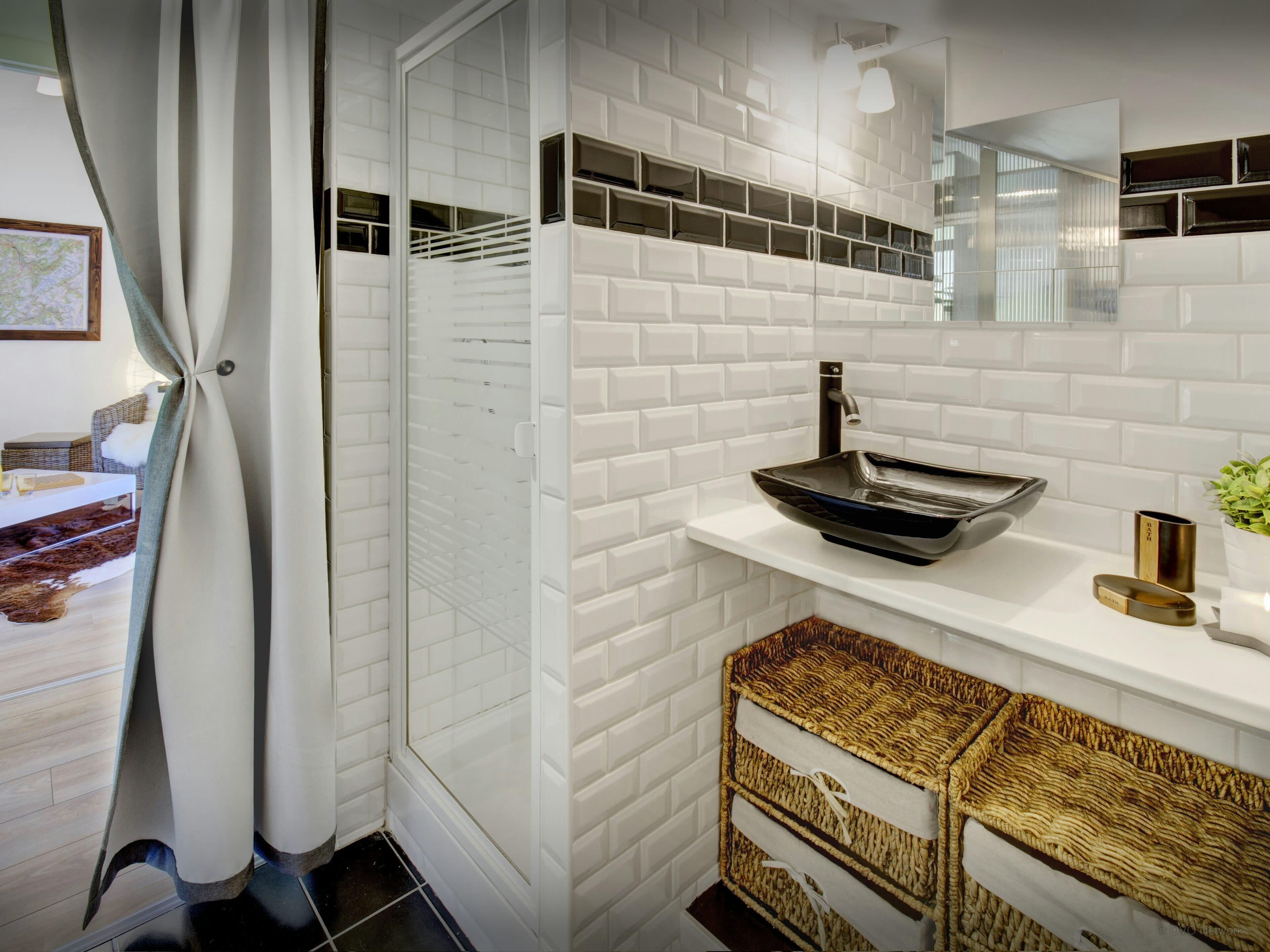 A modern bathroom with white subway tiles, a black vessel sink, and wicker baskets.